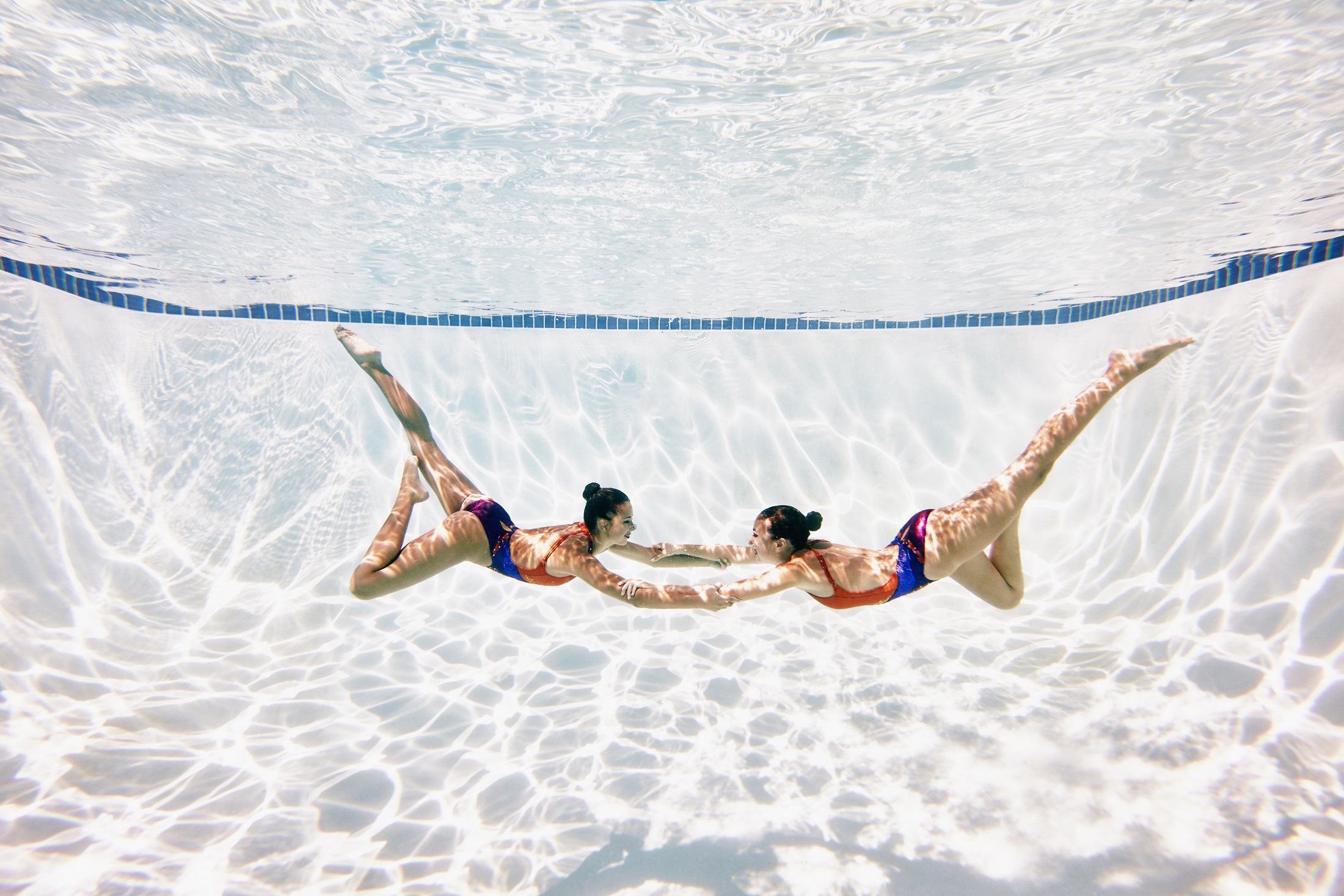 Two female artistic swimmers holding hands underwater performing routine underwater view